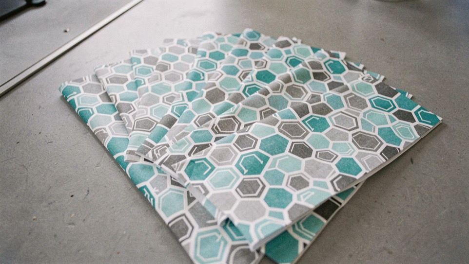 Arrow wrap sheets printed with repeating hexagon patterns in grey, turquoise and white, fanned out on a neutral grey work surface